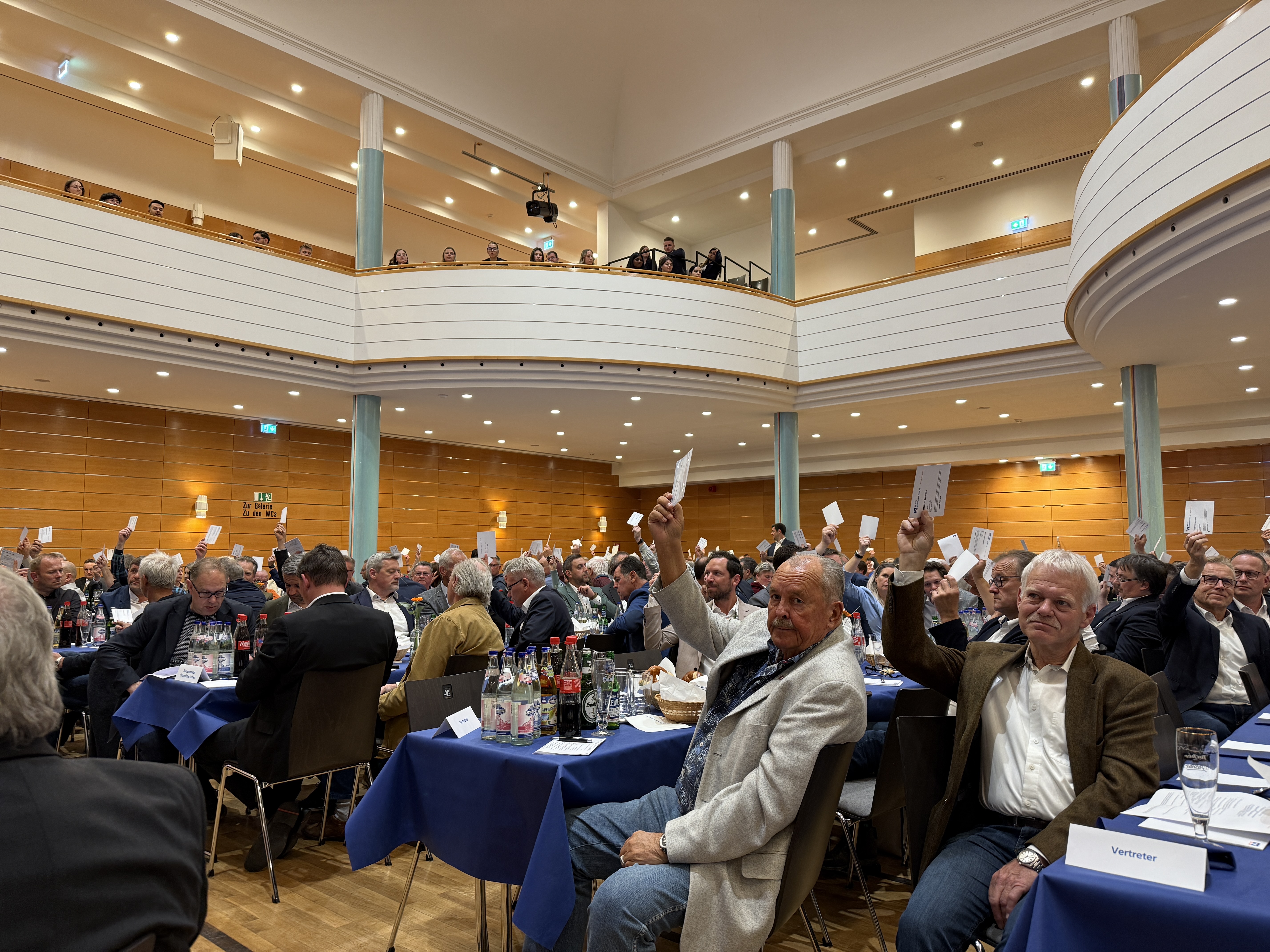 Foto in den Saal - Gäste stimmen mit hochgehaltenen Zetteln ab Foto in den Saal - Gäste stimmen mit hochgehaltenen Zetteln ab